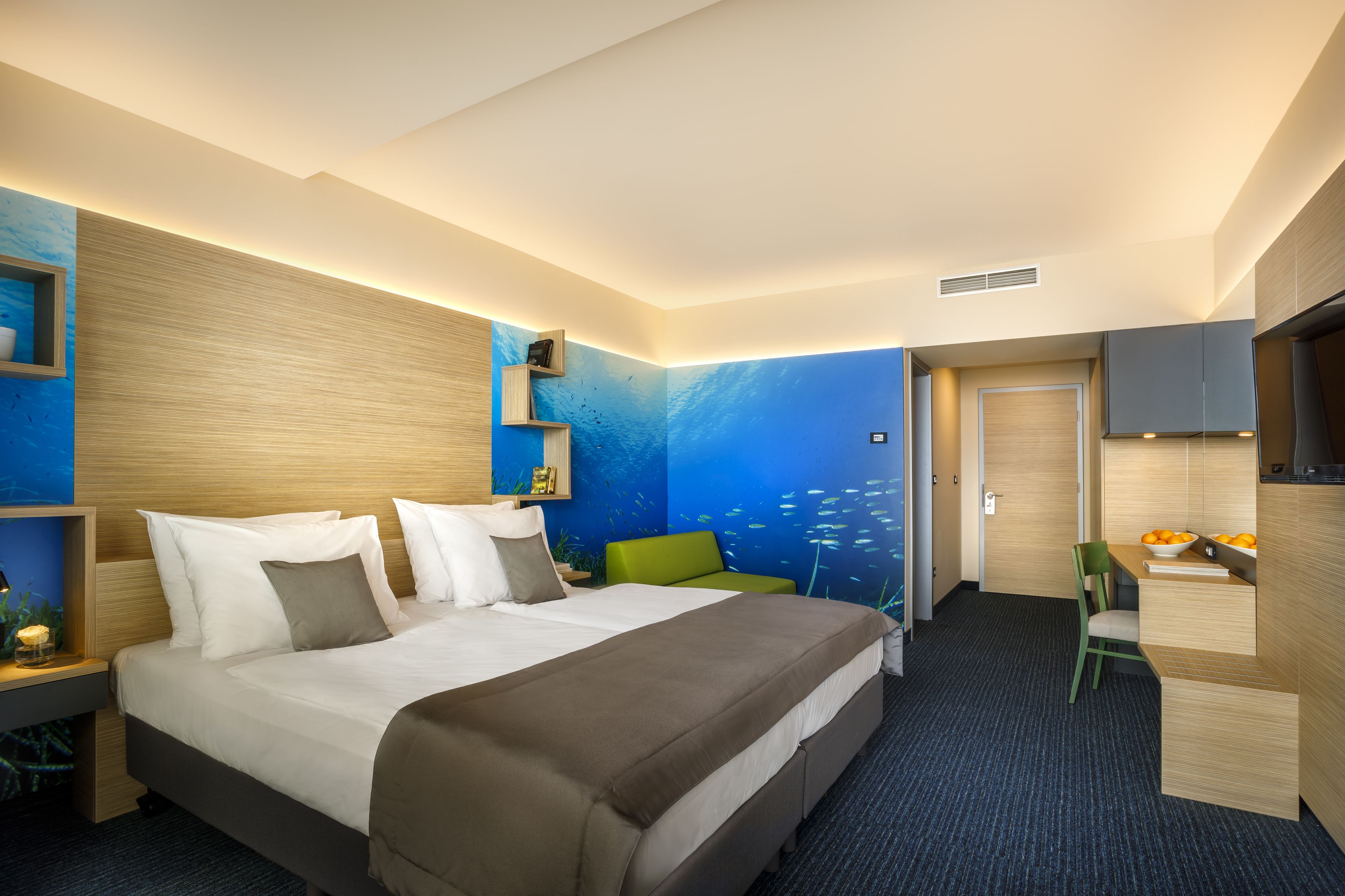 A hotel room with a large bed, a desk with a chair, a TV, and a wall mural.