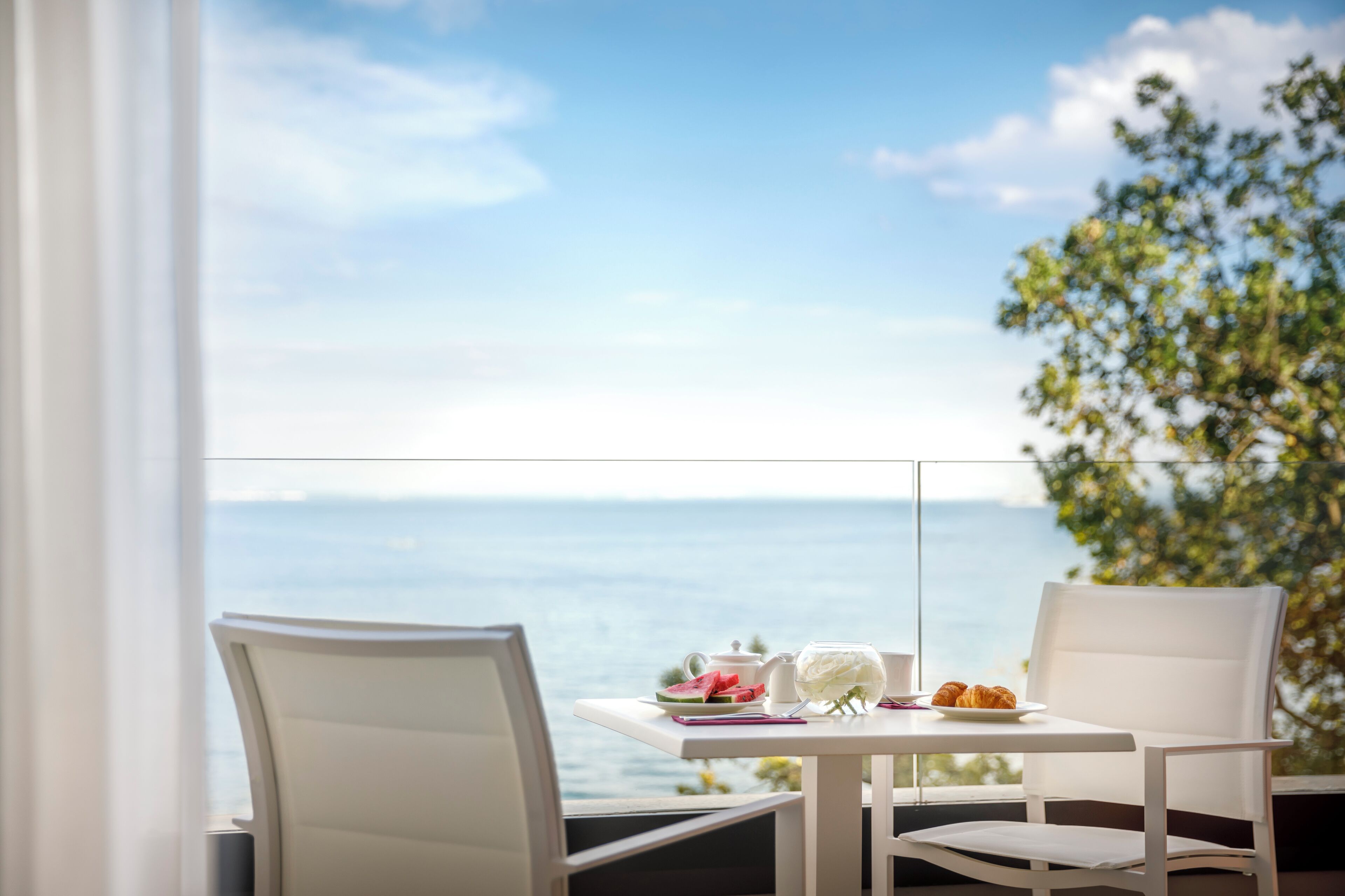 A balcony with a table set for two, overlooking a scenic view of the sea.