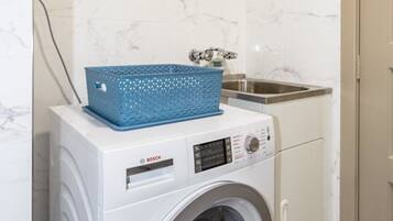 A compact laundry area with a Bosch washing machine, a blue basket, and a stainless steel sink.