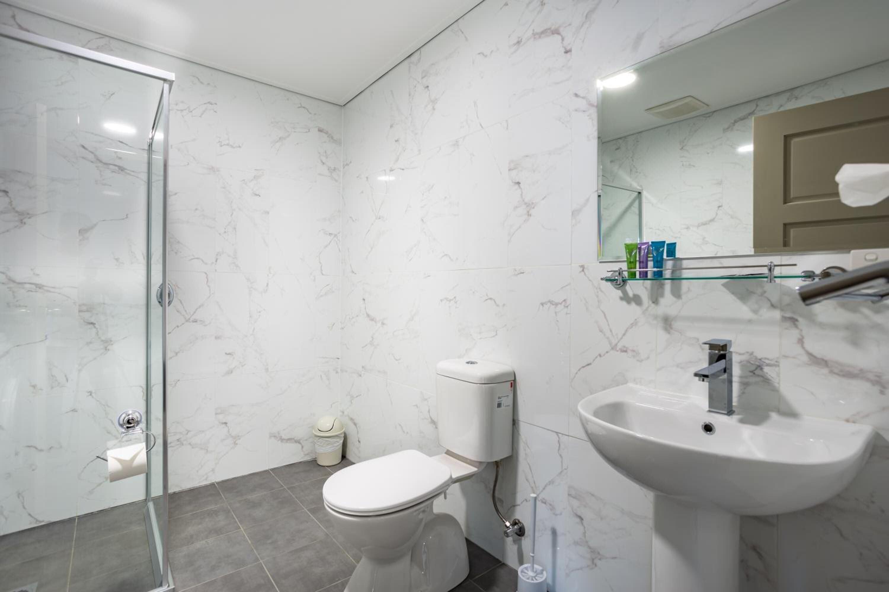 A modern bathroom with a glass shower enclosure, a toilet, and a sink with a marble backsplash.