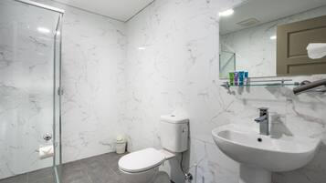 A modern bathroom with a glass shower enclosure, a toilet, and a sink with a marble backsplash.