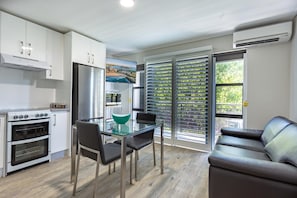 A modern kitchen with white cabinets, a stainless steel refrigerator, and a glass dining table with chairs.