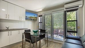 A modern kitchen with white cabinets, a dining table with chairs, and a large window with blinds. - Hamilton on Beaumont (Islington)
