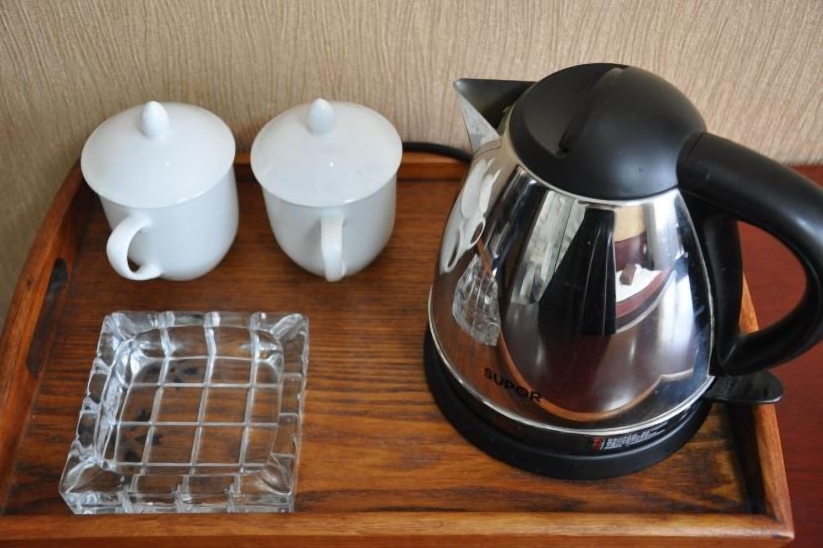 Una tetera negra eléctrica, dos teteras blancas y una bandeja de vidrio sobre una bandeja de madera.