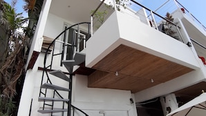 Un edificio moderno con una escalera de caracol, un balcón y un comedor con asientos al aire libre.