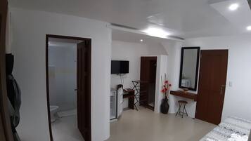 Una habitación de hotel moderna con una cama, un escritorio, una silla, un televisor y un baño visible a través de una puerta abierta.