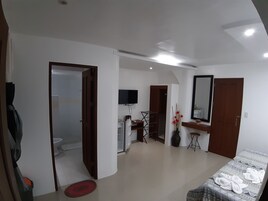 Una habitación de hotel moderna con una cama, un escritorio, una silla, un televisor y un baño visible a través de una puerta abierta.