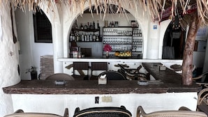 Una zona de bar con sillas de mimbre, techo de paja y estantes llenos de botellas y vasos.