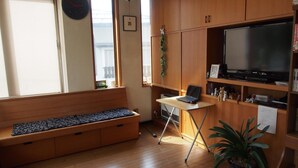 Una habitación con un banco de madera, un escritorio con una computadora portátil, un televisor y una planta en maceta.