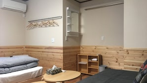 Una habitación con una cama, una mesita, un banco, un espejo y un estante con una toalla y una caja pequeña.