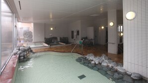 A modern indoor swimming pool with a tiled floor, a rock-lined edge, and a glass partition on one side. - Yuyado Kuttari Onsen Lake Inn (Shintoku)