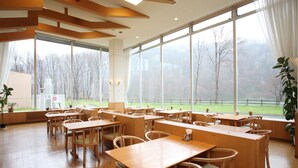 A spacious classroom with wooden desks and chairs, large windows offering a view of trees and a grassy area. - Yuyado Kuttari Onsen Lake Inn (Shintoku)