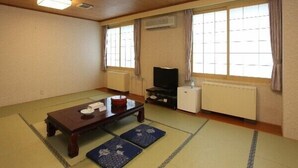 A traditional Japanese-style room with tatami mats, a low wooden table, a television, and a radiator. - Yuyado Kuttari Onsen Lake Inn (Shintoku)
