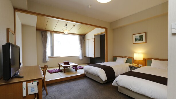 A hotel room with two beds, a desk with a television, a small table, and a window with curtains. - Yuyado Kuttari Onsen Lake Inn (Shintoku)