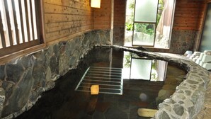 A stone-walled hot tub with a wooden interior, a metal rack, and a stone bench. - Ryokan Kichiman (Kochi)