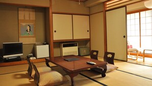 A traditional Japanese room with tatami flooring, a low table, chairs, a television, and a sliding door. - Ryokan Kichiman (Kochi)