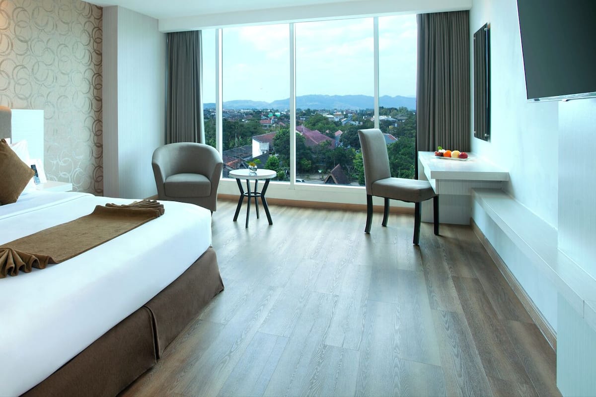 Ein Hotelzimmer mit einem großen Bett, zwei Sesseln, einem kleinen Tisch und Blick auf die Stadt.