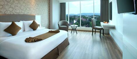 Habitación de hotel con una cama grande, dos sillones, una mesita y vistas a la ciudad.