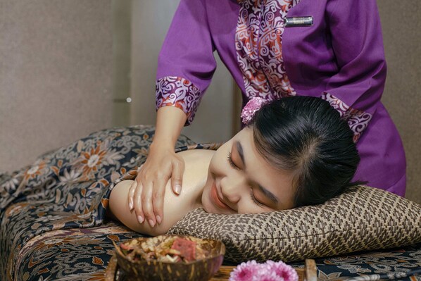A person receiving a massage in a room with patterned bedding and a decorative bowl on the side. - Platinum Adisucipto Hotel & Conference (Depok)