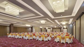 A conference room with rows of tables and chairs, chandeliers, and a patterned carpet.