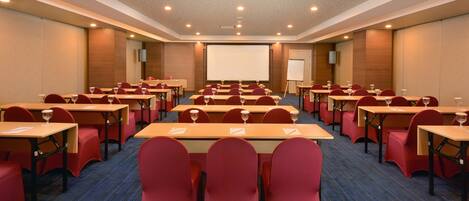 A conference room with rows of tables and chairs, a projector screen, and a whiteboard.