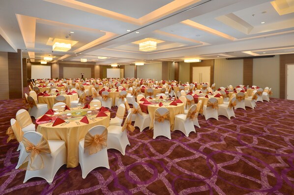Un salón de banquetes con mesas redondas, sillas blancas y manteles rojos.