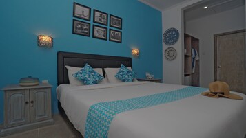 A bedroom with a bed, a nightstand, a dresser, and a wall with framed pictures and decorative plates.