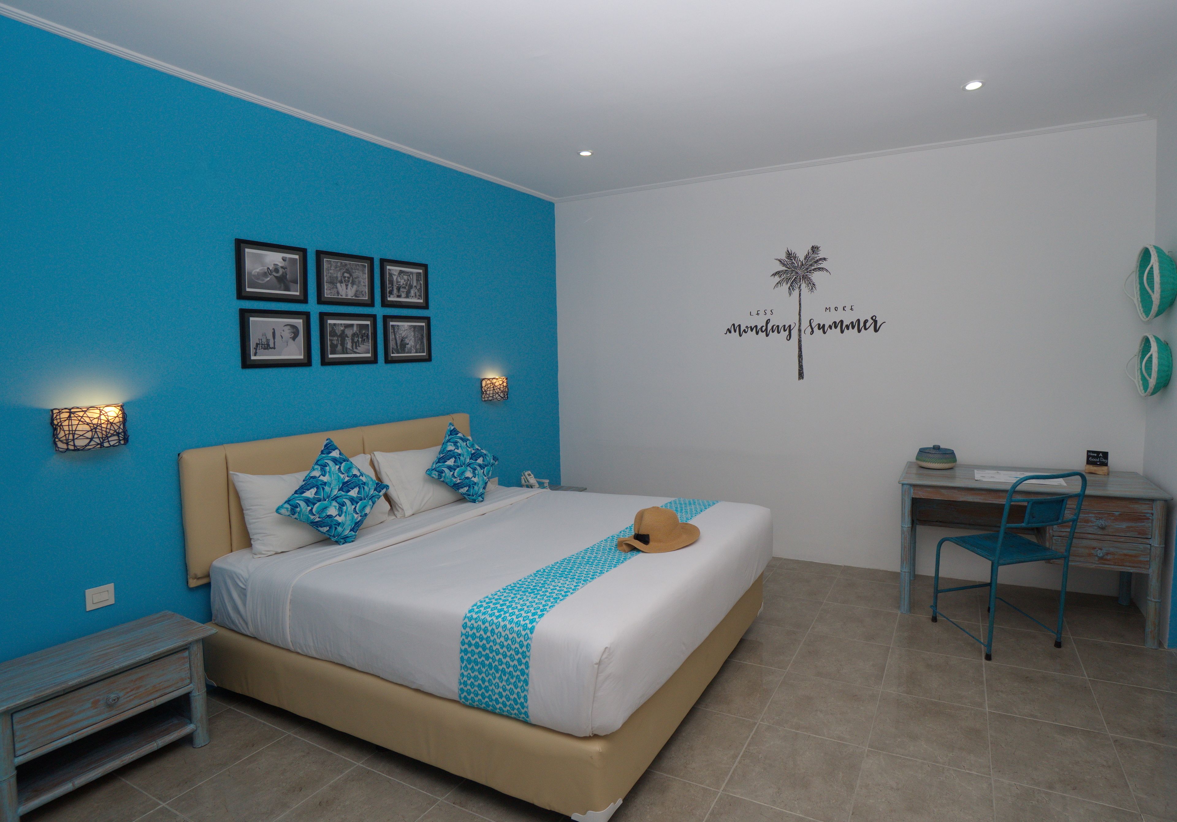 Un dormitorio con cama, escritorio y silla. Hay cuadros en la pared, un adhesivo decorativo y una mesita de noche con una lámpara.