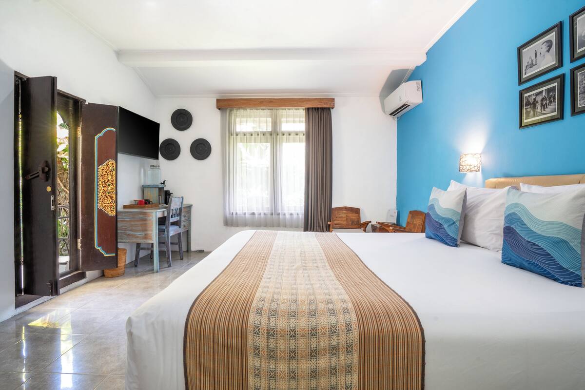 A hotel room with a large bed, a desk, a chair, a TV, and a window with curtains.