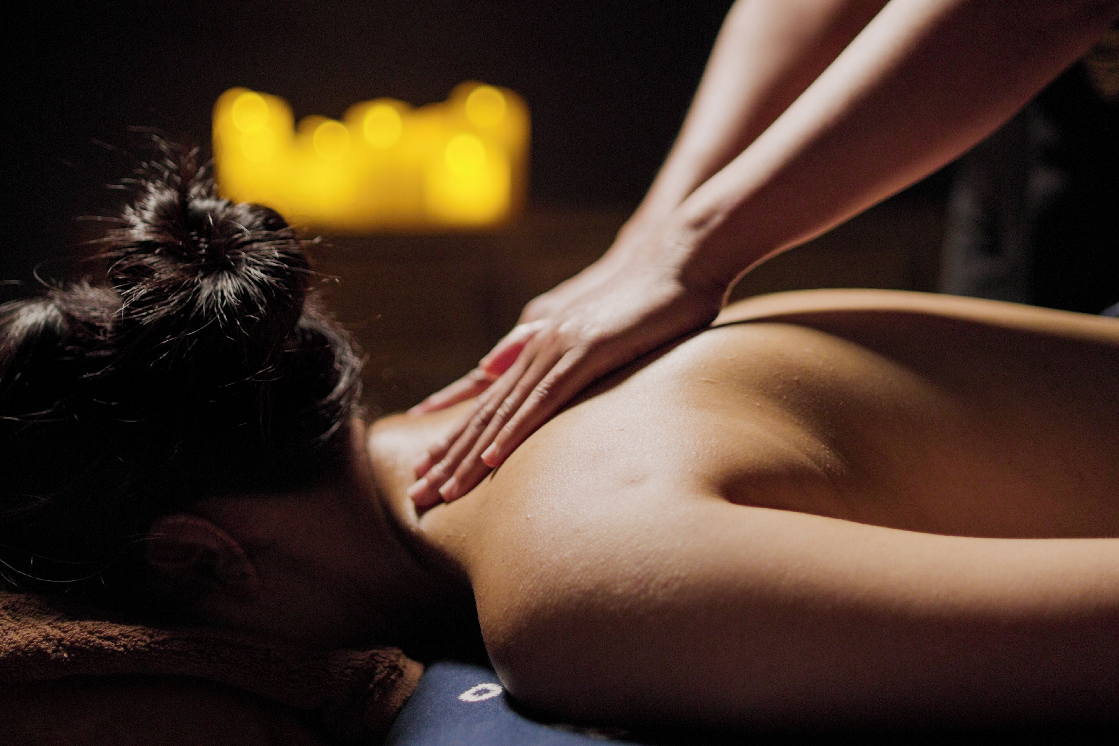 A person receiving a massage in a dimly lit room with a soft glow in the background.