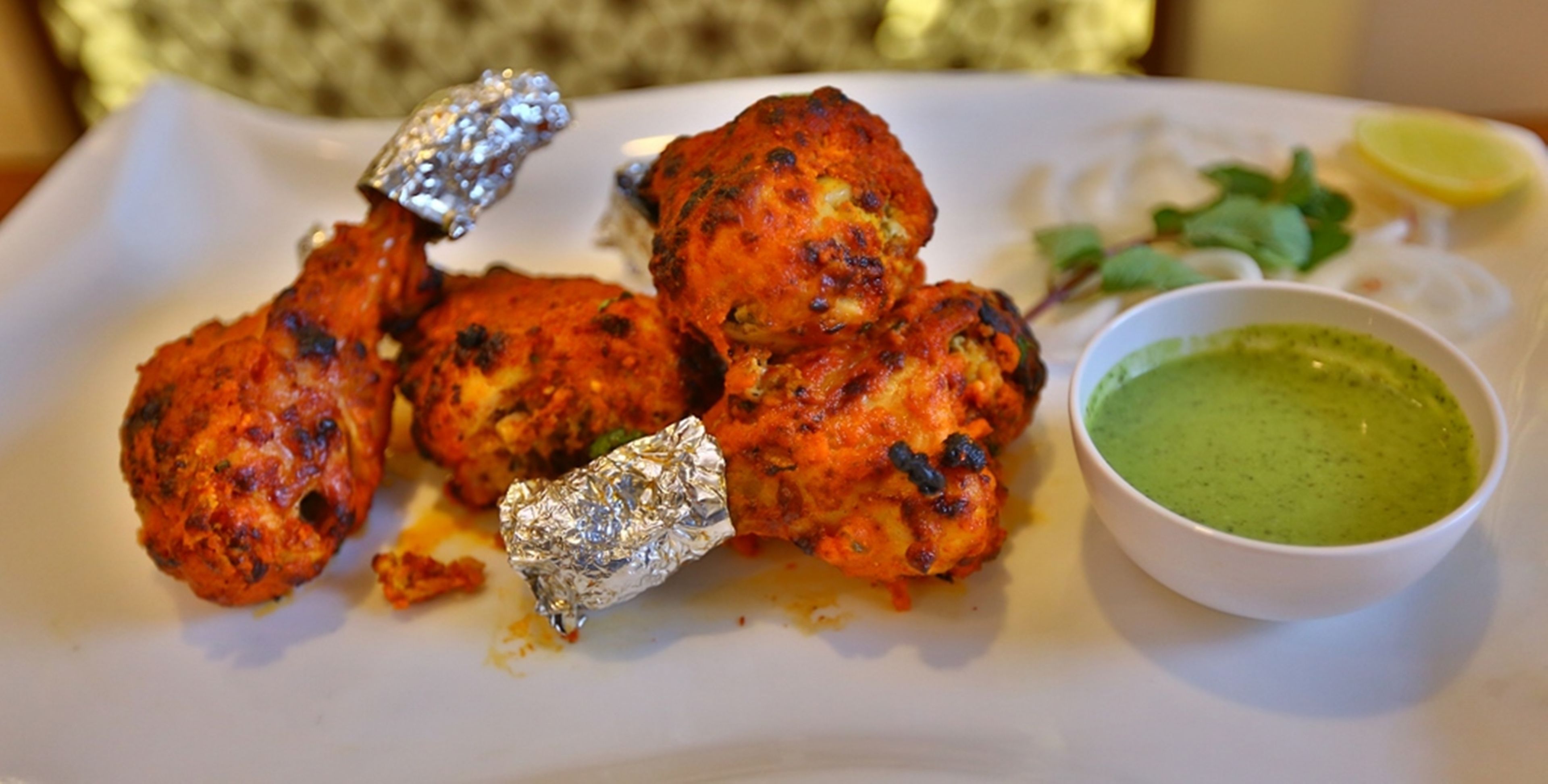 A plate of tandoori chicken with foil-wrapped pieces and a bowl of green chutney.
