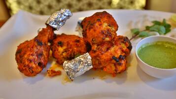 A plate of tandoori chicken with foil-wrapped pieces and a bowl of green chutney.