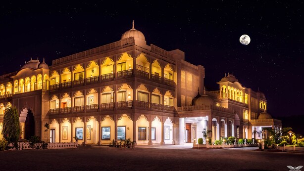 Un edificio grande y ornamentado con múltiples cúpulas y balcones, iluminado en la noche.