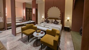 Habitación de hotel con cama, dos sillones, una mesita con fruta, ventilador de techo y espejo.