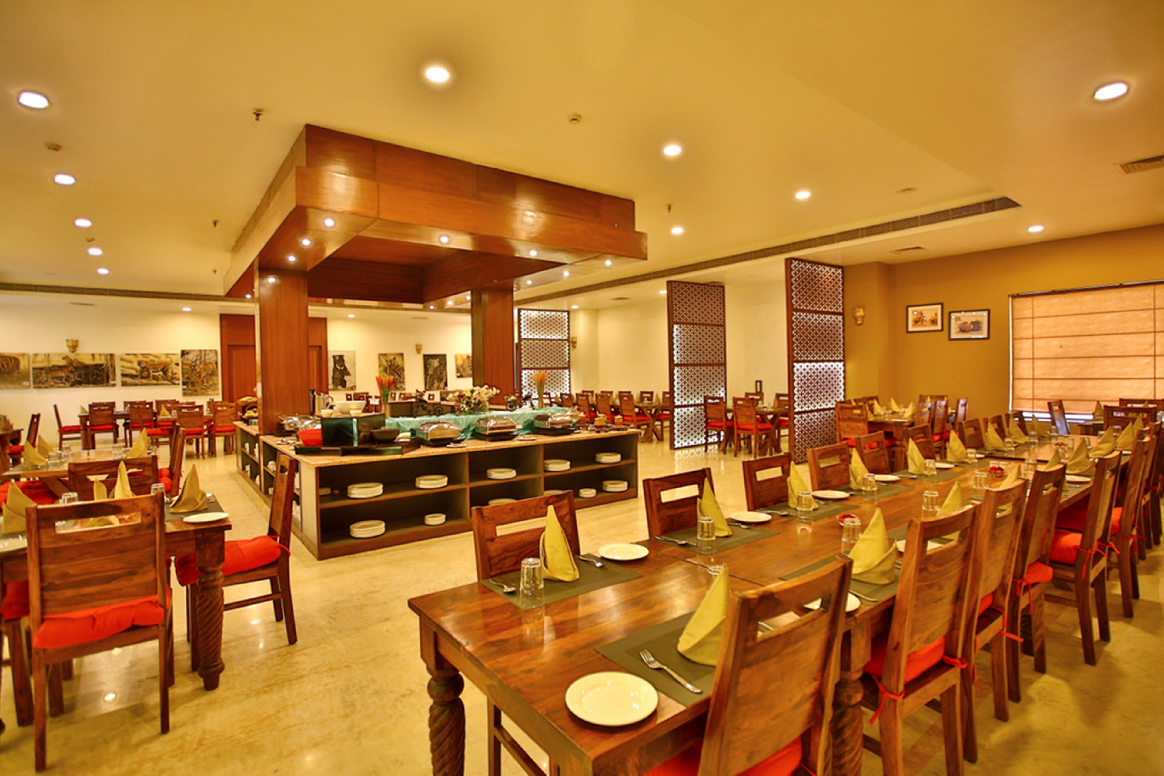 Un restaurant spacieux, doté de nombreuses tables et chaises, d’un buffet central et d’un plafond haut avec des luminaires encastrés.