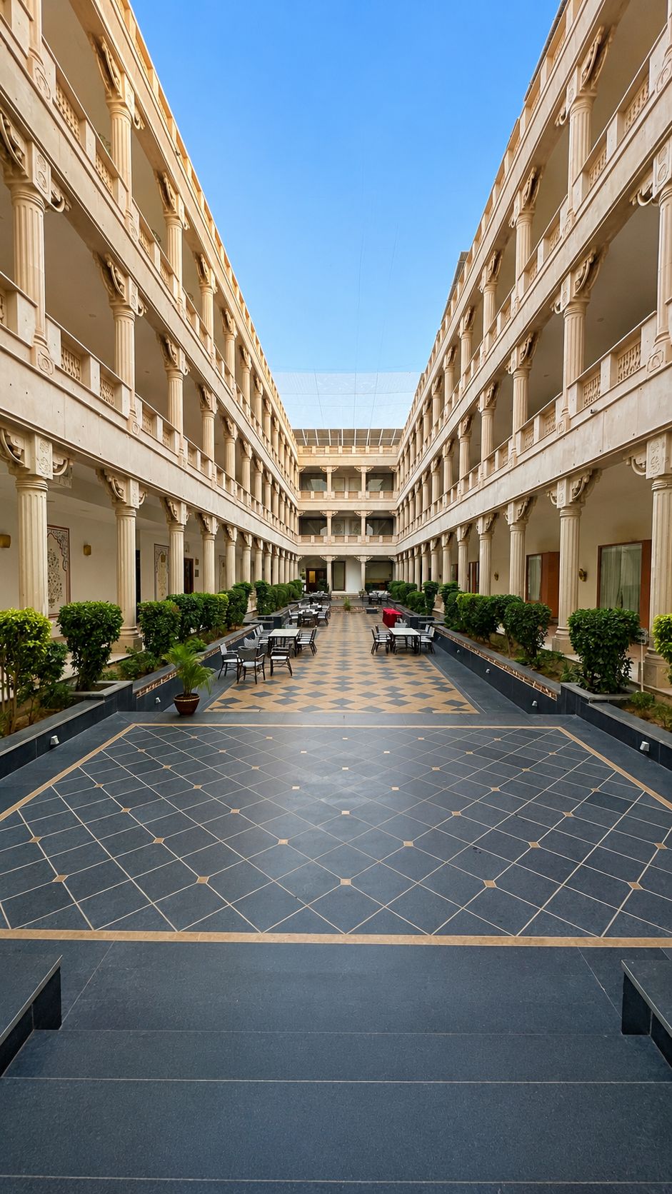 A hotel courtyard with a central open space, columns, and potted plants.