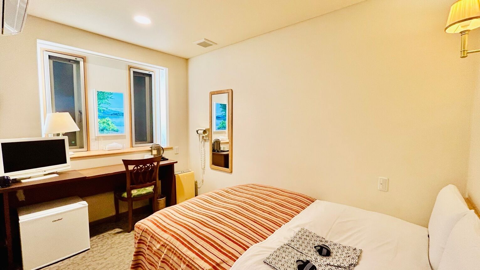 Ein Hotelzimmer mit einem Bett, einem Schreibtisch mit Computer, einem Sessel, einem kleinen Kühlschrank, einem Fenster mit Blick und einem Spiegel.