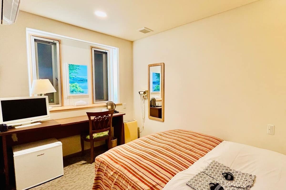 Une chambre d’hôtel comprenant un lit, un bureau avec un ordinateur, une chaise, un petit réfrigérateur, une fenêtre avec vue et un miroir.