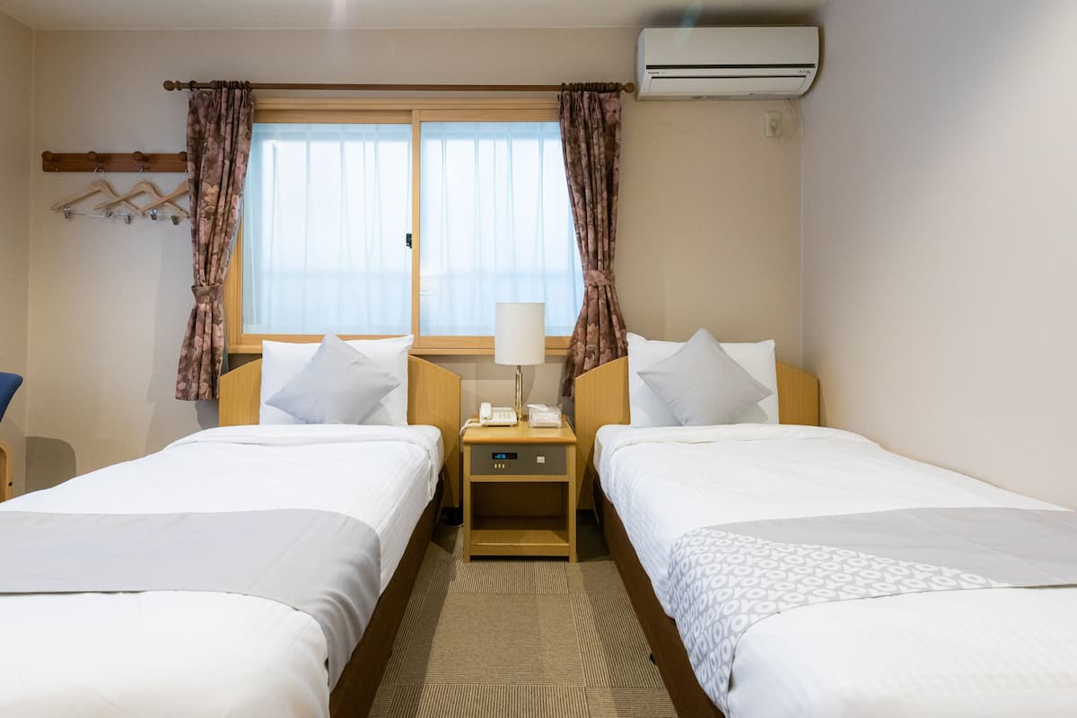 Une chambre d’hôtel avec deux lits simples, une table de chevet avec une lampe, un téléphone et un climatiseur fixé au mur.