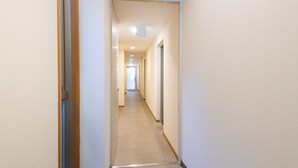 A narrow, well-lit hallway with a carpeted floor and white walls, leading to a door at the end.