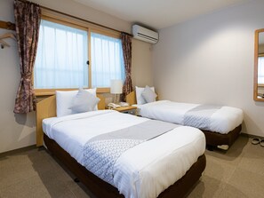 Habitación de hotel con dos camas, una mesita de noche con lámpara, equipo de aire acondicionado y ventana con cortinas.