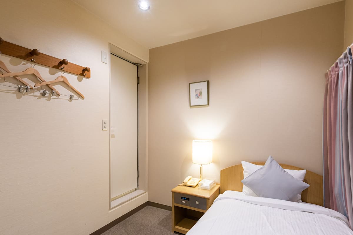 Une chambre d’hôtel comprenant un lit, une table de chevet avec une lampe, un téléphone et un porte-manteau avec des cintres.