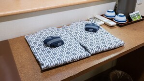 A neatly arranged hotel room with a bed, a small table with a tissue box, a remote control, a kettle, and a tray with teapots.