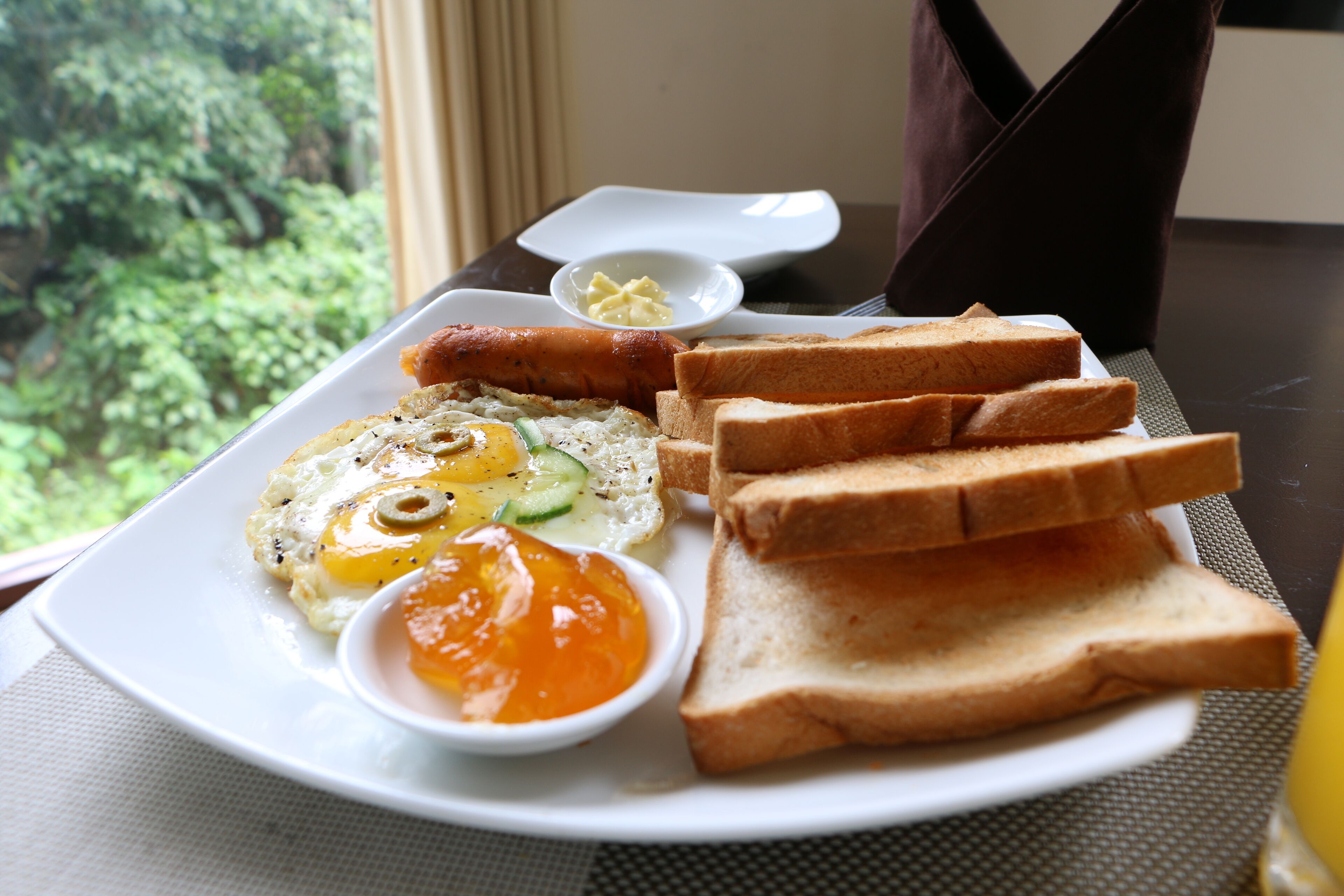 En frukosttallrik med ägg, rostat bröd och smör, placerad på ett bord med utsikt över grönskan.