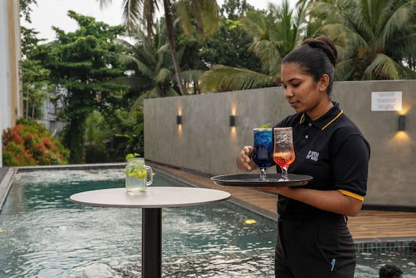 A person serving drinks by a poolside with a tropical backdrop.