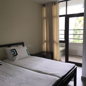 A hotel room with a bed, a nightstand, a window with curtains, and a view of greenery outside.