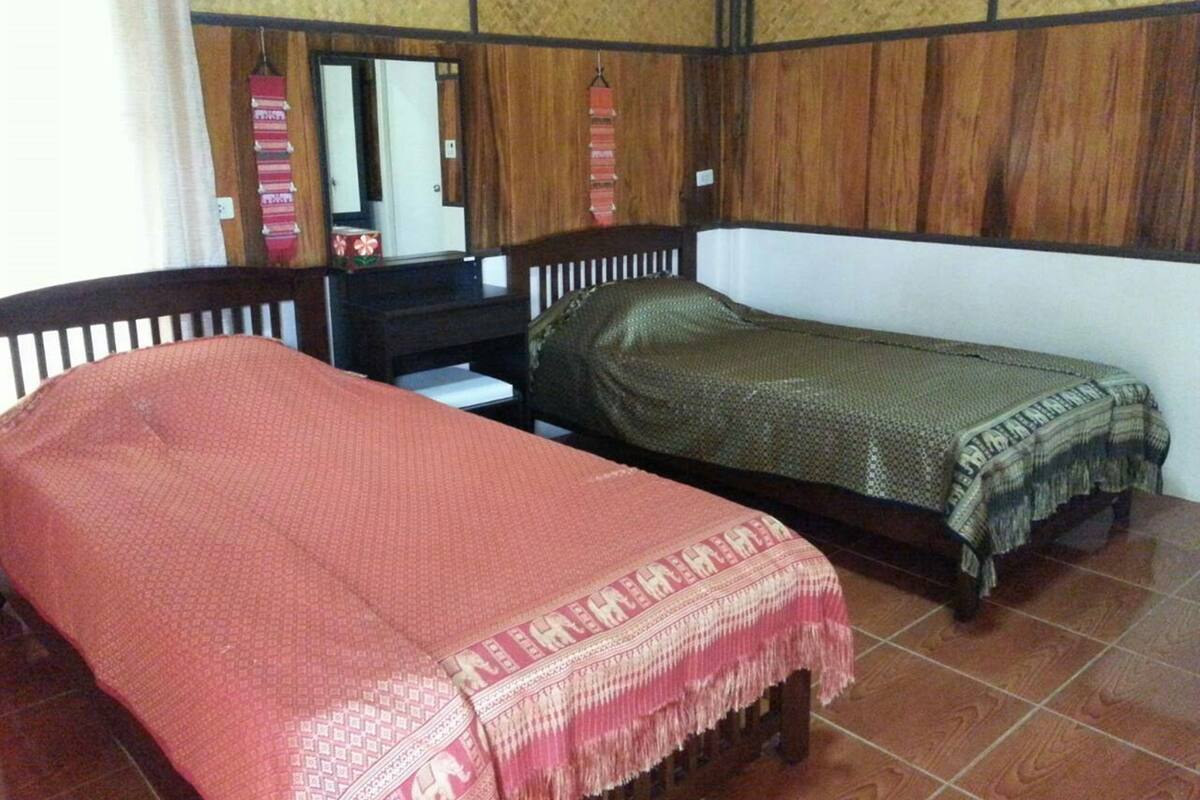A room with two single beds, a wooden desk, a mirror, and a patterned wall.