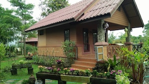 A two-story house with a tiled roof, a porch with a railing, and a garden with various plants and flowers. - Maesai Doi View Resort (Mae Sai)