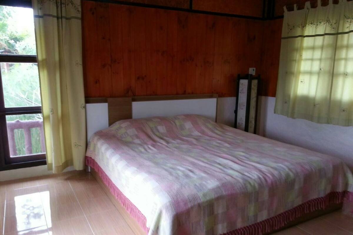 A bedroom with a wooden headboard, a bed with a patterned bedspread, and a window with curtains.