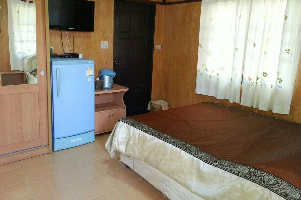 A compact room with a bed, a small kitchenette with a refrigerator, a television, and a door.